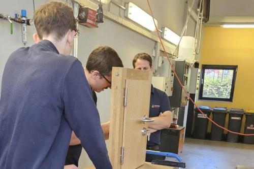 Zu sehen sind drei Feuerwehrmänner, die üben, eine Wohnungstür zu öffnen