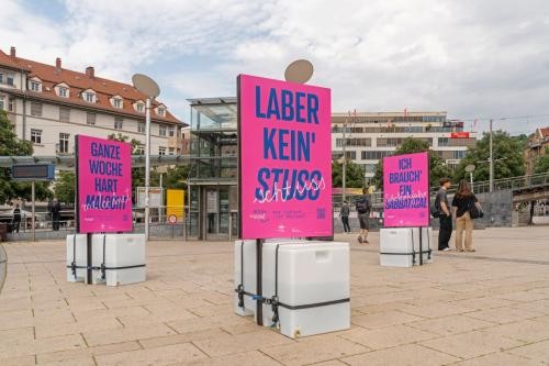 drei Stelen mit pinken Plakaten stehen auf einem großen Platz. Auf dem mittleren Plakat steht "Laber kein' Stuss"
