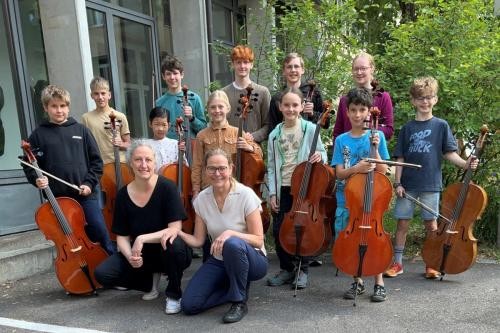 Junge Cellistinnen und Cellisten auf einem Gruppenbild mit Instrumenten und ihren Lehrerinnen