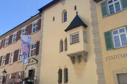 Gelbe angestrichener Turm mit Erker, umgeben von zwei Wohnhäusern