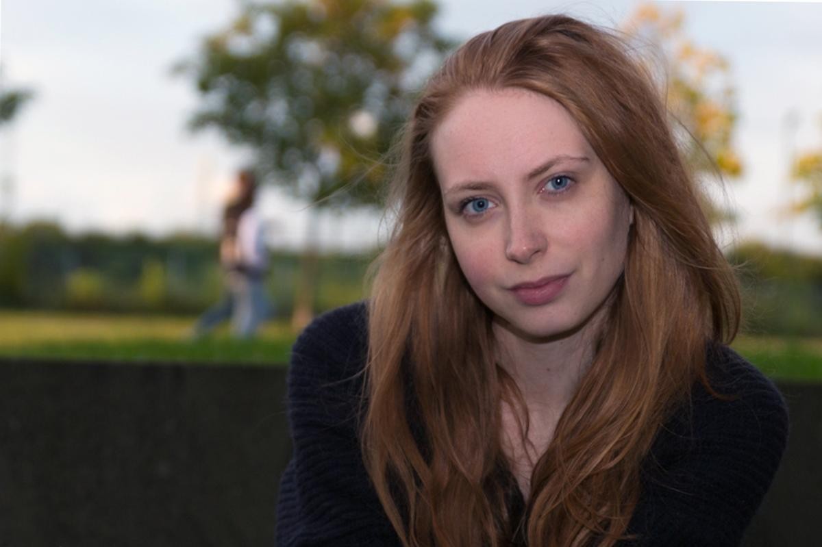 Junge Frau schaut in die Kamera mit grüner Natur im Hintergrund 