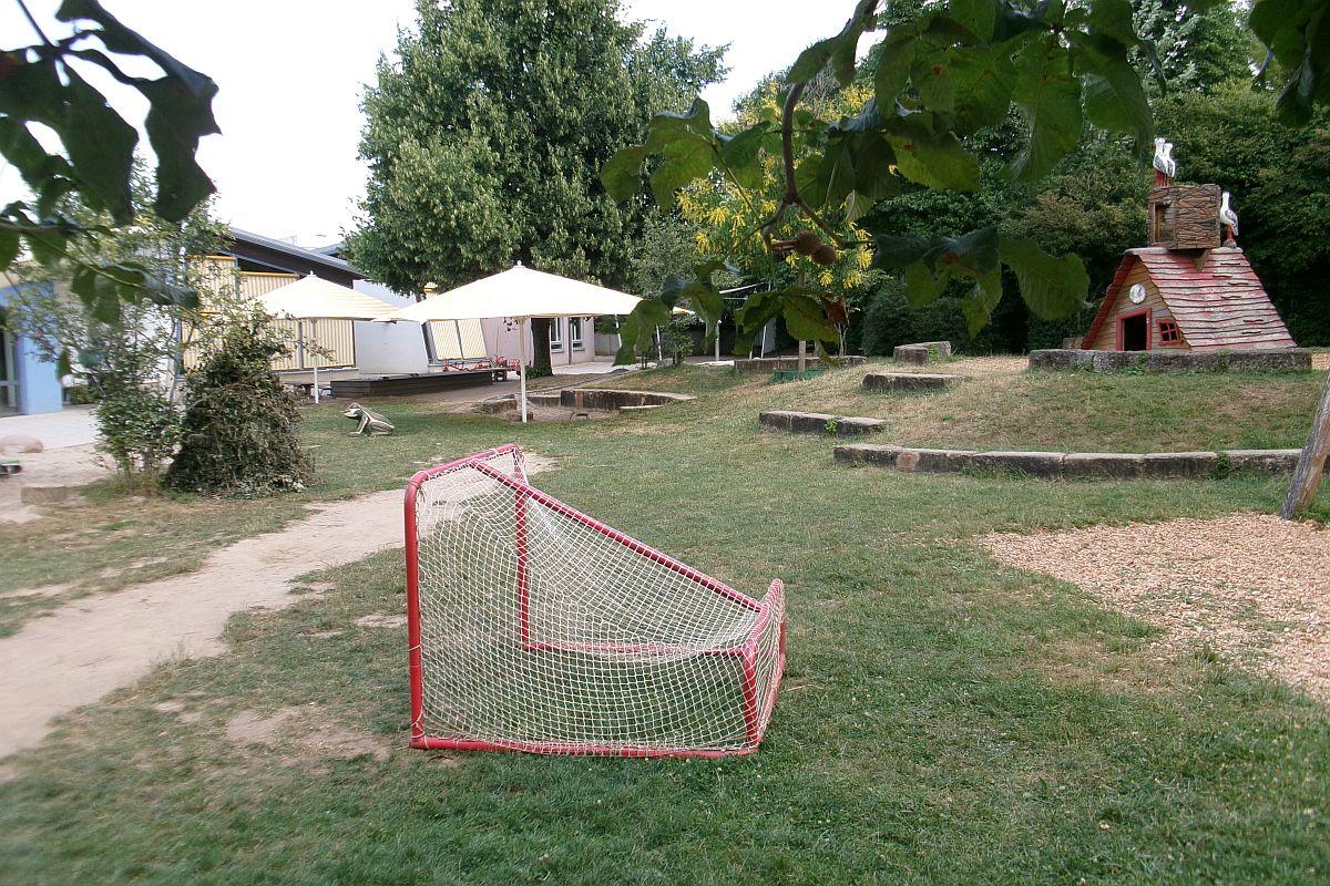 Das Fußballtor, das Spielhaus und der Sandkasten mit geöffneten Sonnenschirmen im Garten der städtischen Kita Auenweg