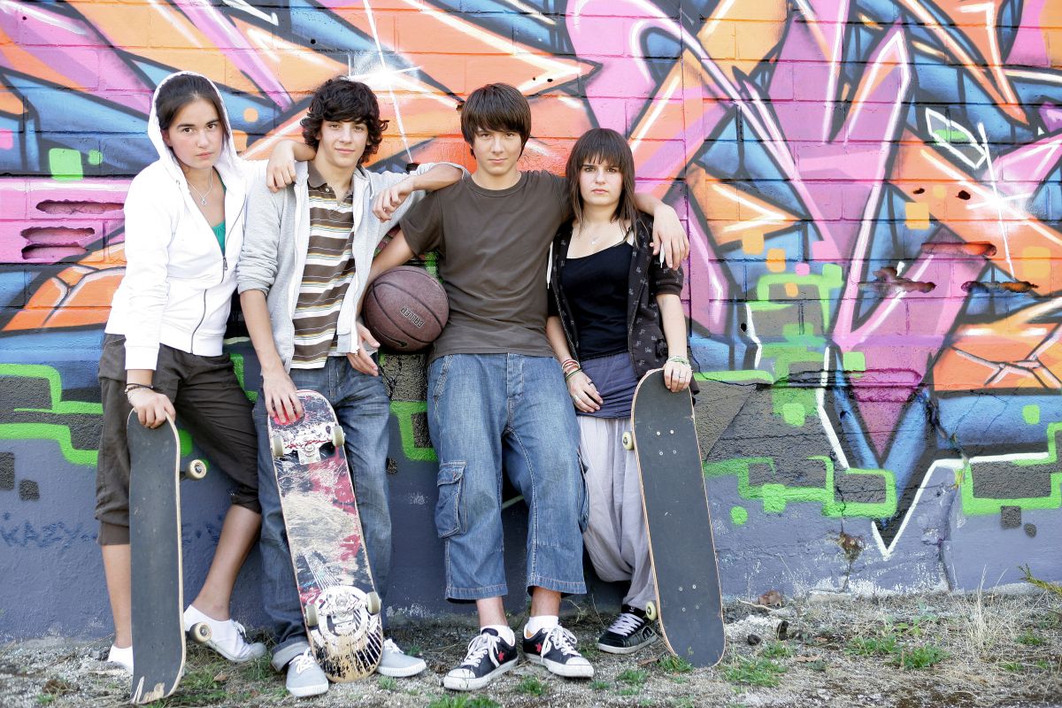 Jugendliche mit Ball und Skateboards vor einer Graffity-Wand 