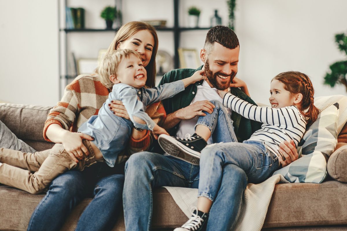 Mutter, Vater und zwei Kinder albern auf dem Sofa herum.
