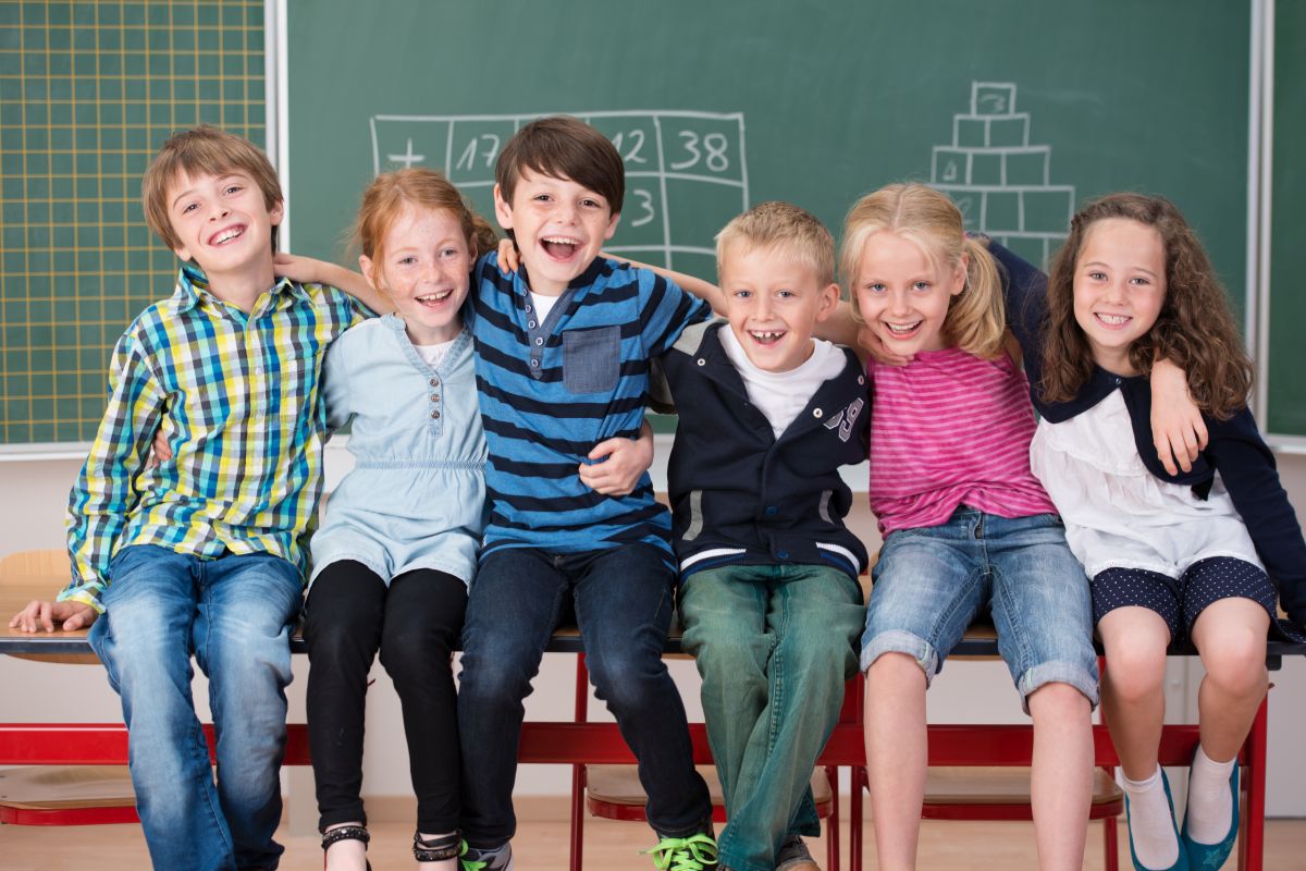 Lachende Grundschulkinder vor einer Schultafel.