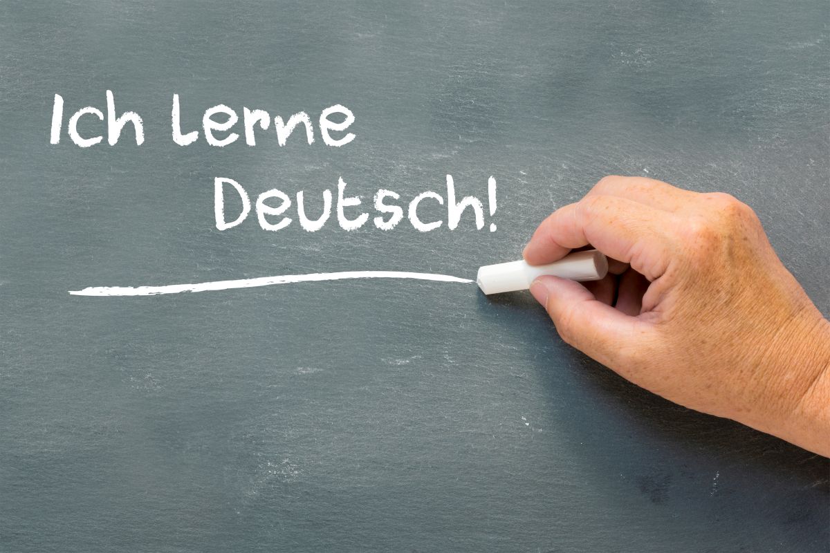 Deutschkurs Eine Hand schreibt an eine Tafel: "Ich lerne Deutsch!"
