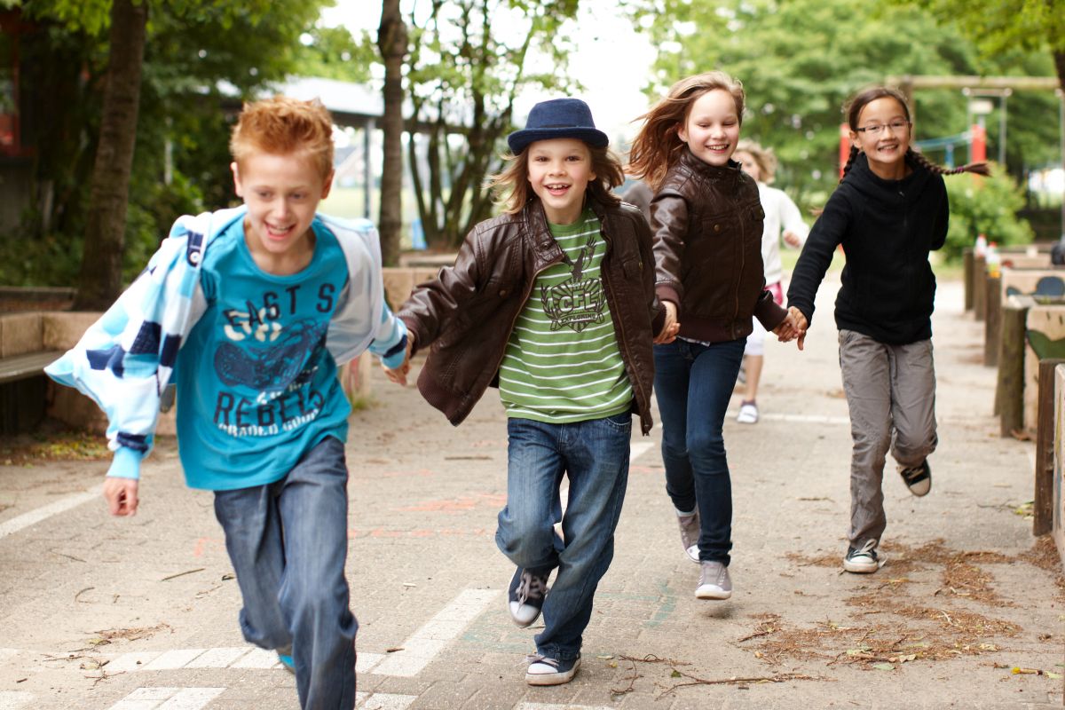 Jungs und Mädchen rennen Hand in Hand über den Schulhof.