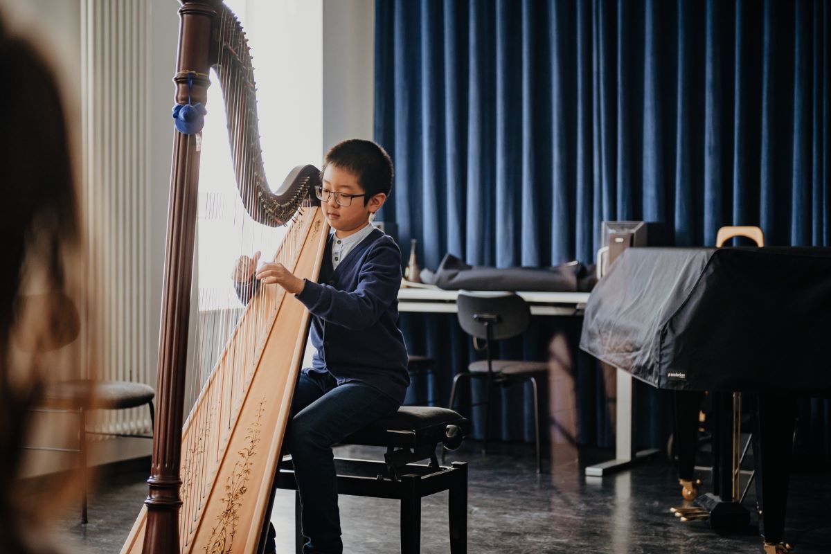 Harfe, Städtische Musikschule Esslingen © Sabine Watzko Junge mit dunklen Haaren und Brille spielt, auf einem Klavierhocker sitzend, auf einer Harfe