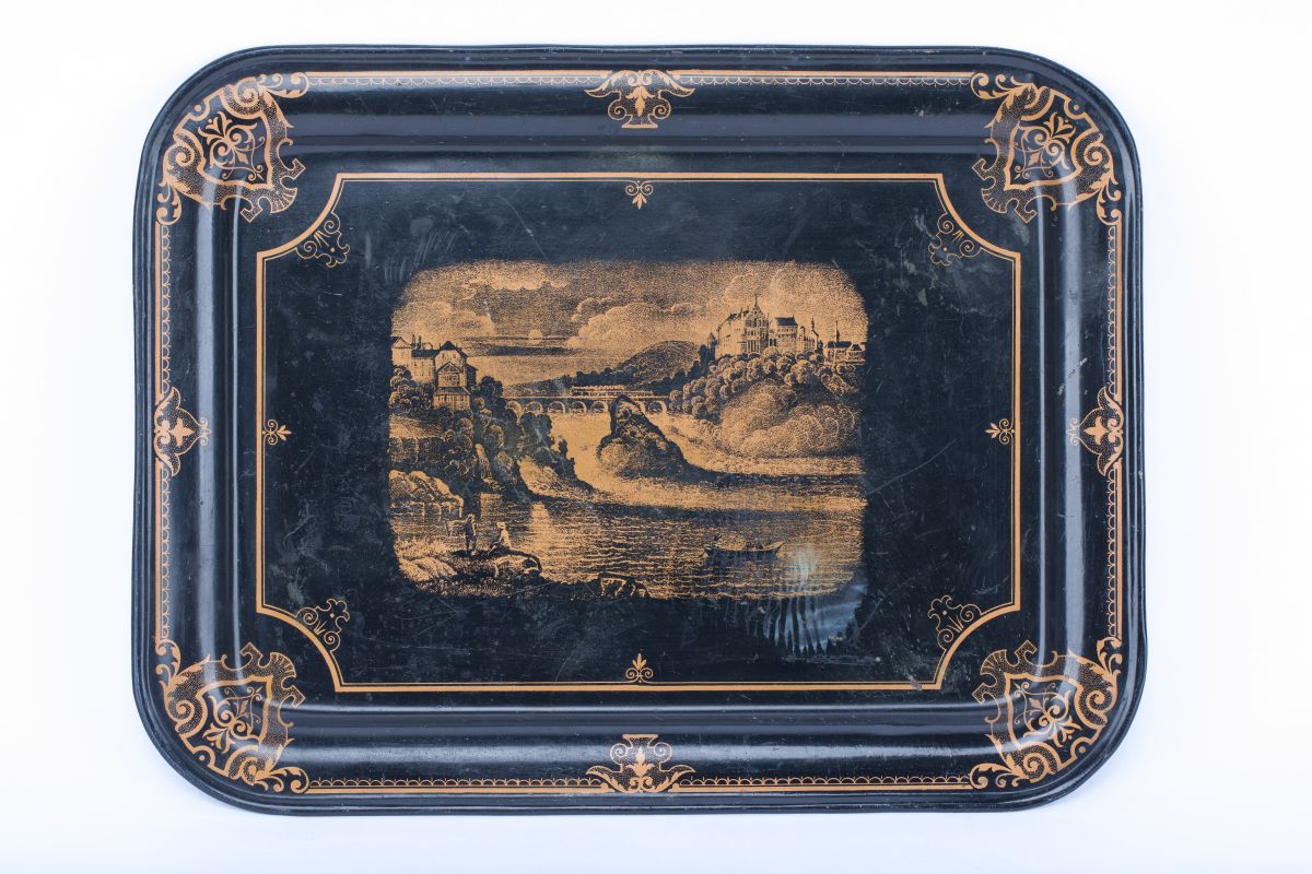 Schwarzes Tablett mit abgerundeten Ecken. Darauf sind orangene Verzierungen und eine orangefarbene Ansicht des Rheinfalls gedruckt.
