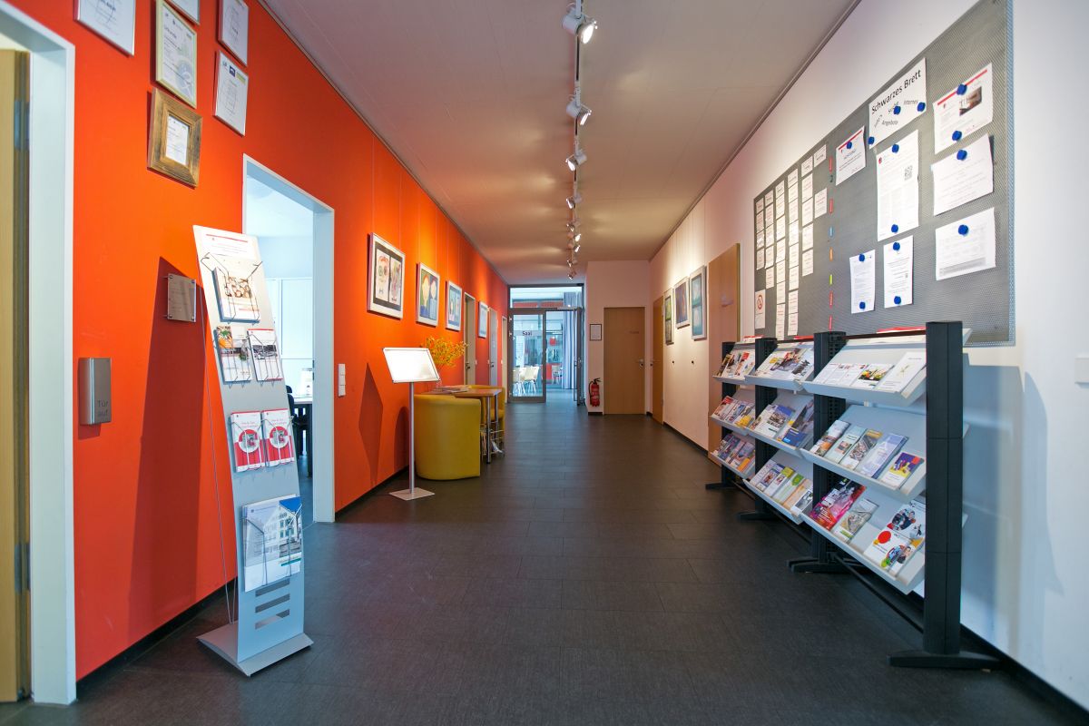 Blick in den Flur mit Ständern mit Informationsmaterial und Sitzmöglichkeit.