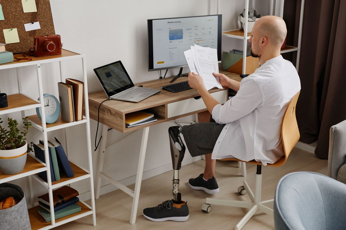 Wohnen und Arbeiten Mann mit Beinprothese am Schreibtisch in seiner Wohnung
