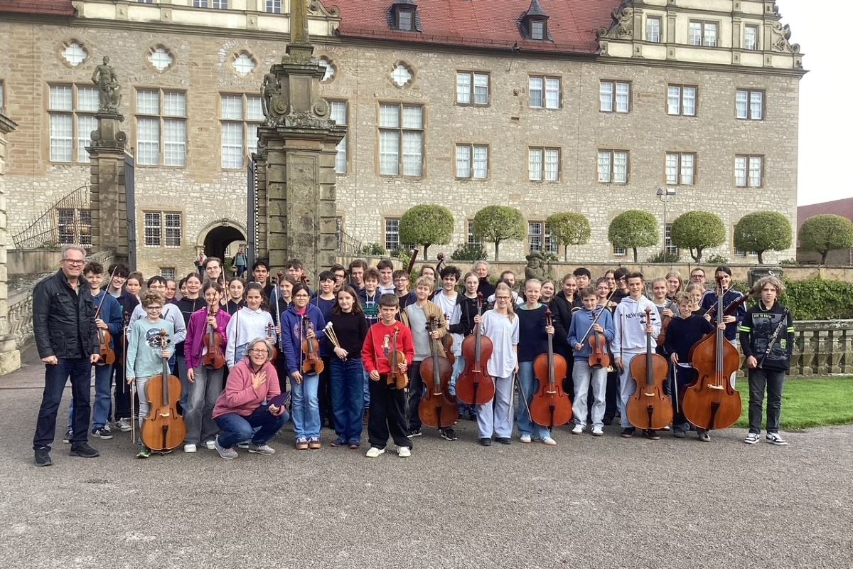 Gruppe von rund 50 jungen Leuten mit ihren Instrumenten stehen in einem Park vor vor einem Schluss