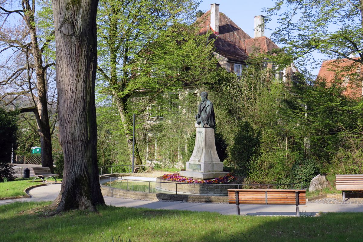 Grünanlage, Bäume, Bänke und Bronzebüste umgeben von einem Brunnenbecken