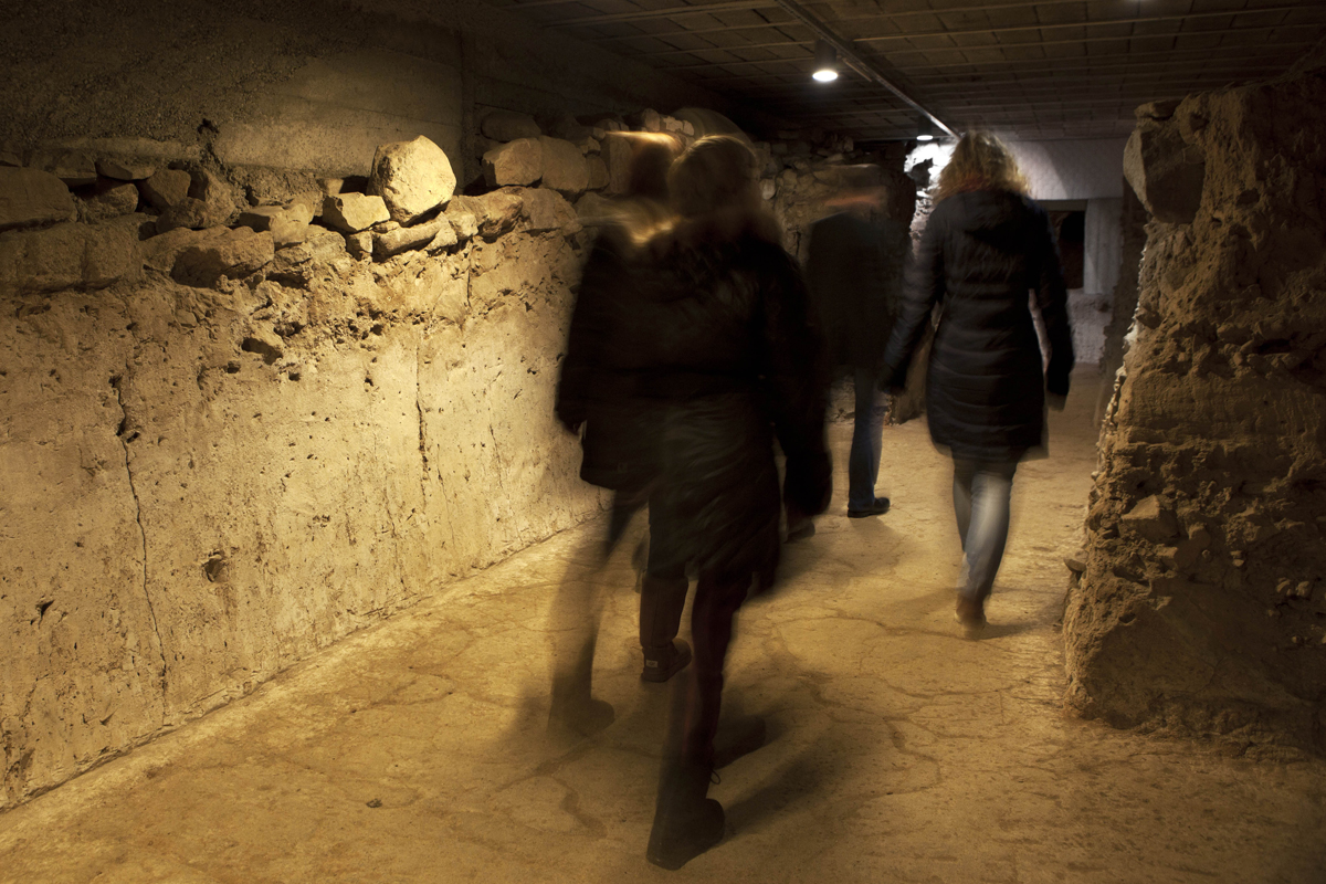 Im Ausgrabungsmuseum: Ausgegrabene Wand mit Besucherinnen und Besuchern von hinten. Im Ausgrabungsmuseum: Ausgegrabene Wand mit Besucherinnen und Besuchern von hinten.