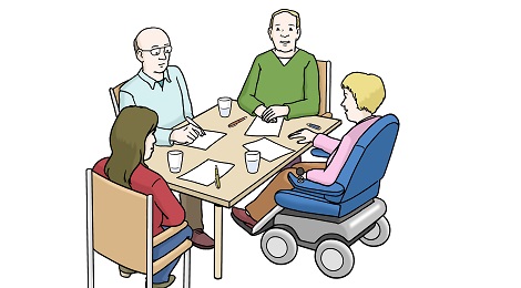 Frau mit Elektrorollstuhl sitzt mit einer Arbeitsgruppe am Tisch