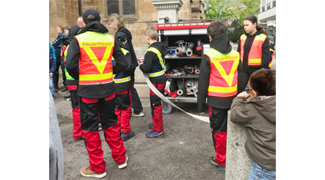 Die Kindergruppe "Feuerflitzer" mit einem Schlauch und einem Wagen, in dem Anschluss-Stutzen sichtbar sind.