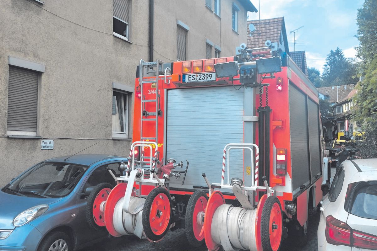 Titel = Tooltip Rotes Löschfahrzeug der Feuerwehr fährt durch eine enge Stelle zwischen zwei rechts und links geparkten Autos