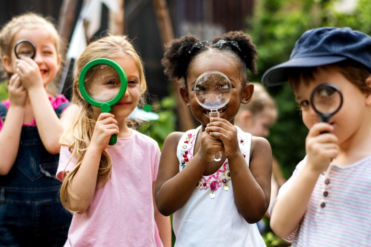 Lupe Vier Kinder mit Lupe schauen durch die Lupe in die Kamera.