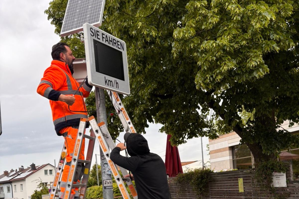 Smiley Installtion des Displays bei Regenwetter, zwei Männer arbeiten auf einer Leiter.
