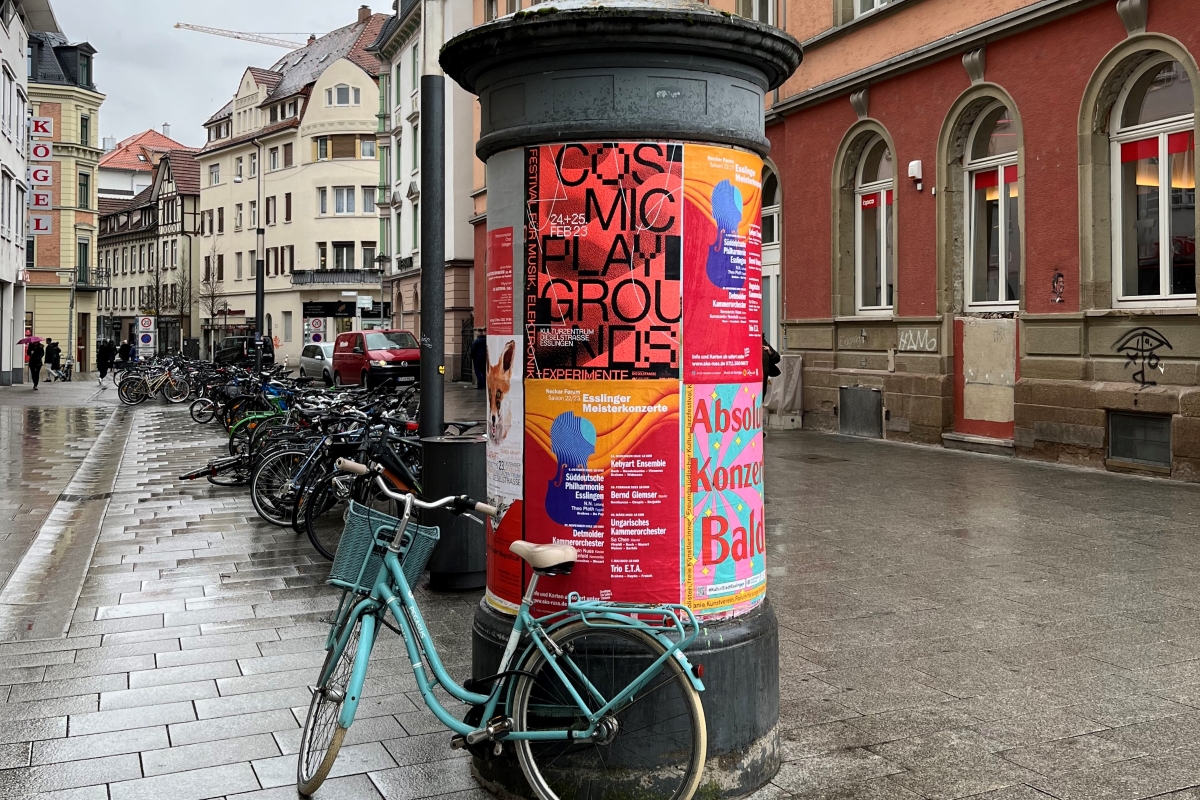 Bunte Plakate an einer Litfaßsäule, davor ein Fahrrad
