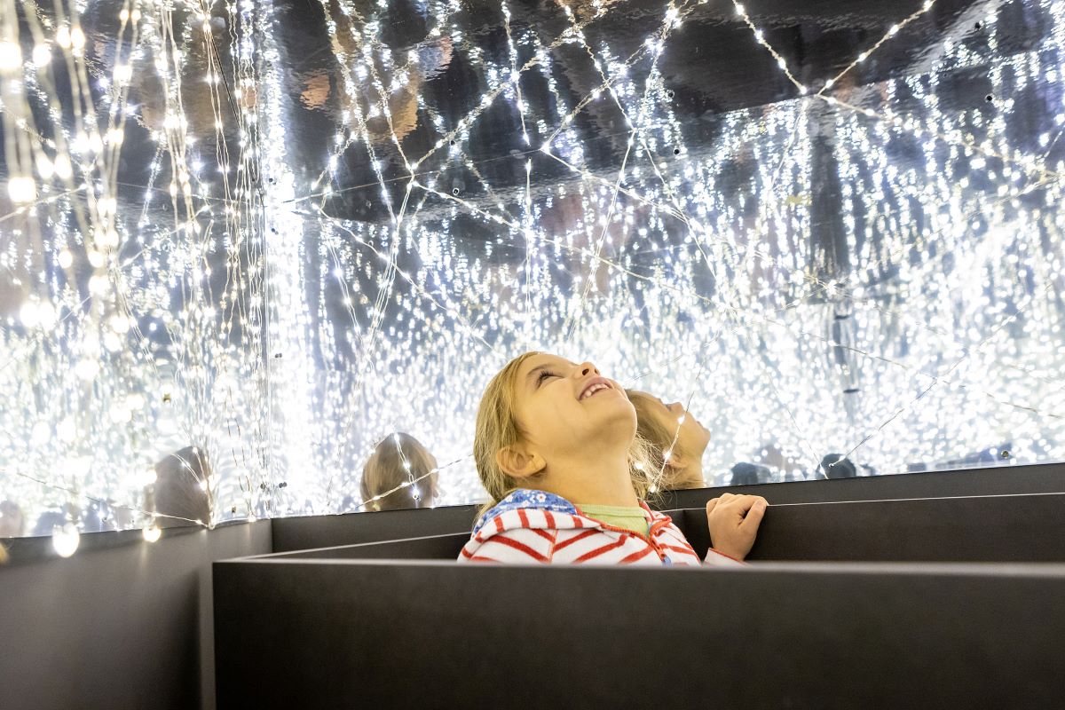 Esslingen nachtaktiv © Ludwigsburg Museum/ Benjamin Stollenberg Mädchen sitzt in dunkler Box und schaut nach oben, in einen Raum voller Lichterketten, der wie ein Sternenhimmel wirkt.