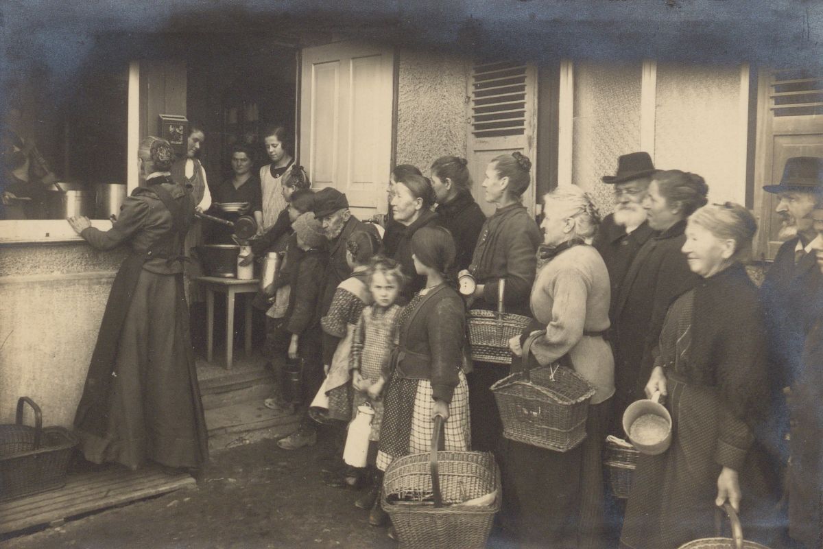 Fotografie Alte Fotografie, viele Frauen und Kinder stehen mit Körben und Töpfen um Essen an.