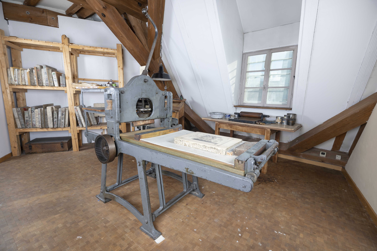 Fotografie: Michael Saile. Ausstellungsraum mit alter Lithopresse und einem Regal mit Lithosteinen.