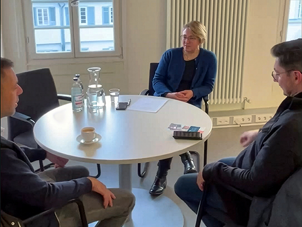 zwei Männer und eine Frau im Gespräch an einem runden Tisch