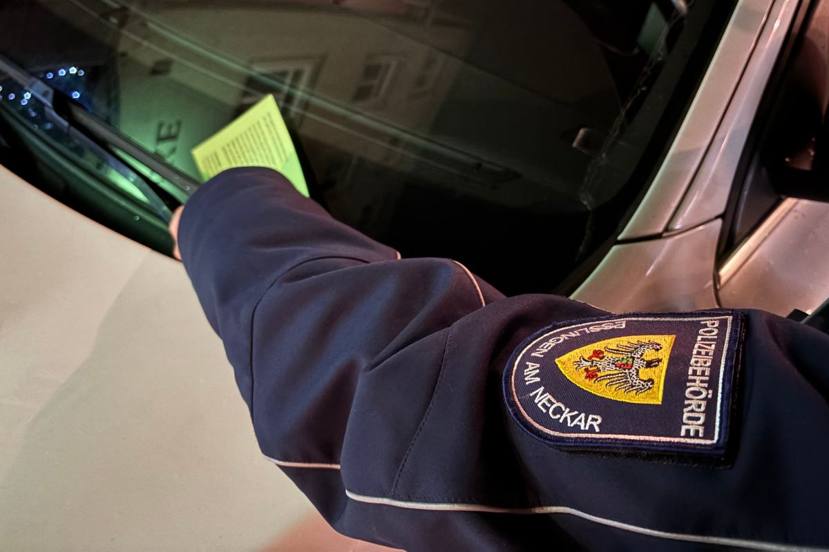 Mitarbeiterin klemmt grünen Zettel an Scheibenwischer, nur der Arm ist zu sehen.