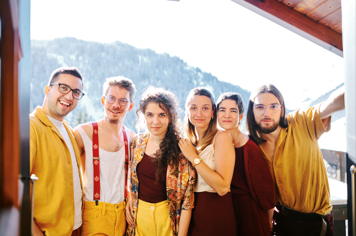 Tzupati Orchestra ©Ella Josephine Campbell drei Frauen und drei Männer in gelber und dunkelroter Kleidung auf einem überdachten Balkon vor einer verschneiten Landschaft