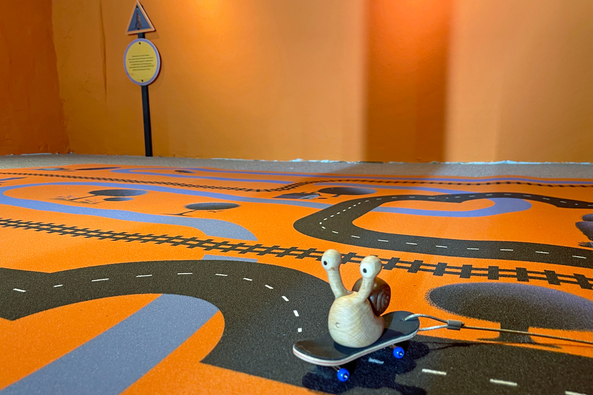 Eine Schnecke fährt auf einem Skateboard auf dem "Autobahn"-Teppichboden.