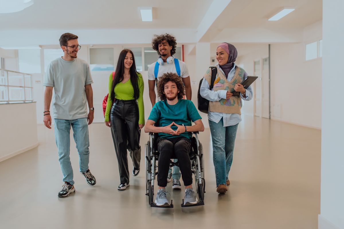 Bildung und Engagement Studierende gehen mit einem Rollstuhlfahrer über einen Flur