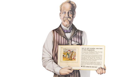 Pappaufsteller in Form eines älteren Mannes, der ein aufgeschlagenes Buch zeigt.