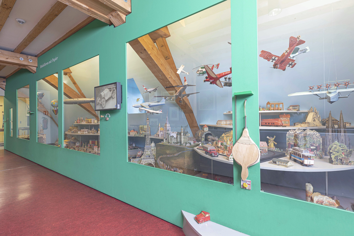 Fotografie: Michael Saile. Große Vitrine mit zahlreichen Kartonmodellen, unter anderem von Flugzeugen, Bauwerken, Schiffen.