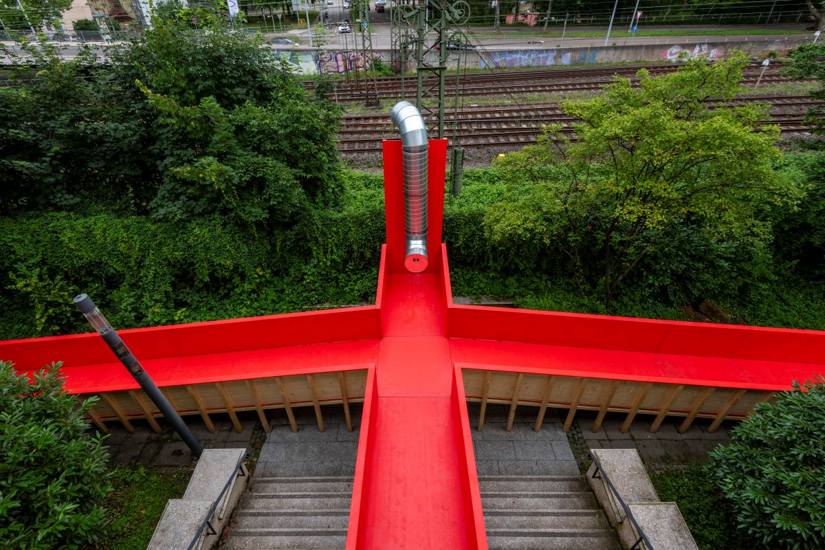 Kollektiv Plus X, Niederflureinstieg, Intervention in spiegelrot, 2024 © Frank Kleinbach kreuzförmig angeordnete rote Rampen aus Holz, von oben fotografiert