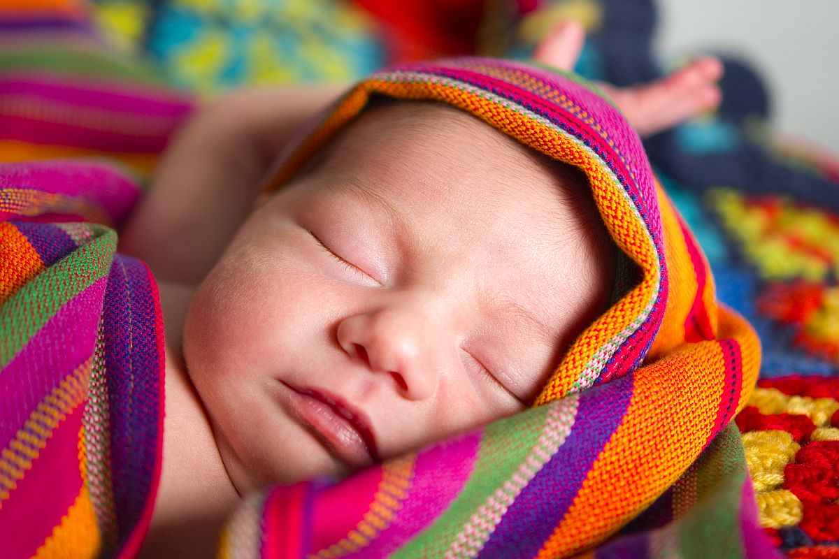 Baby Schlafendes Neugeborenes in buntes Tuch gehüllt.