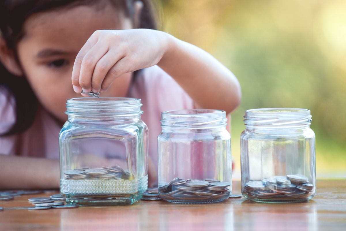 Mädchen sortiert Münzen in unterschiedliche Gläser.