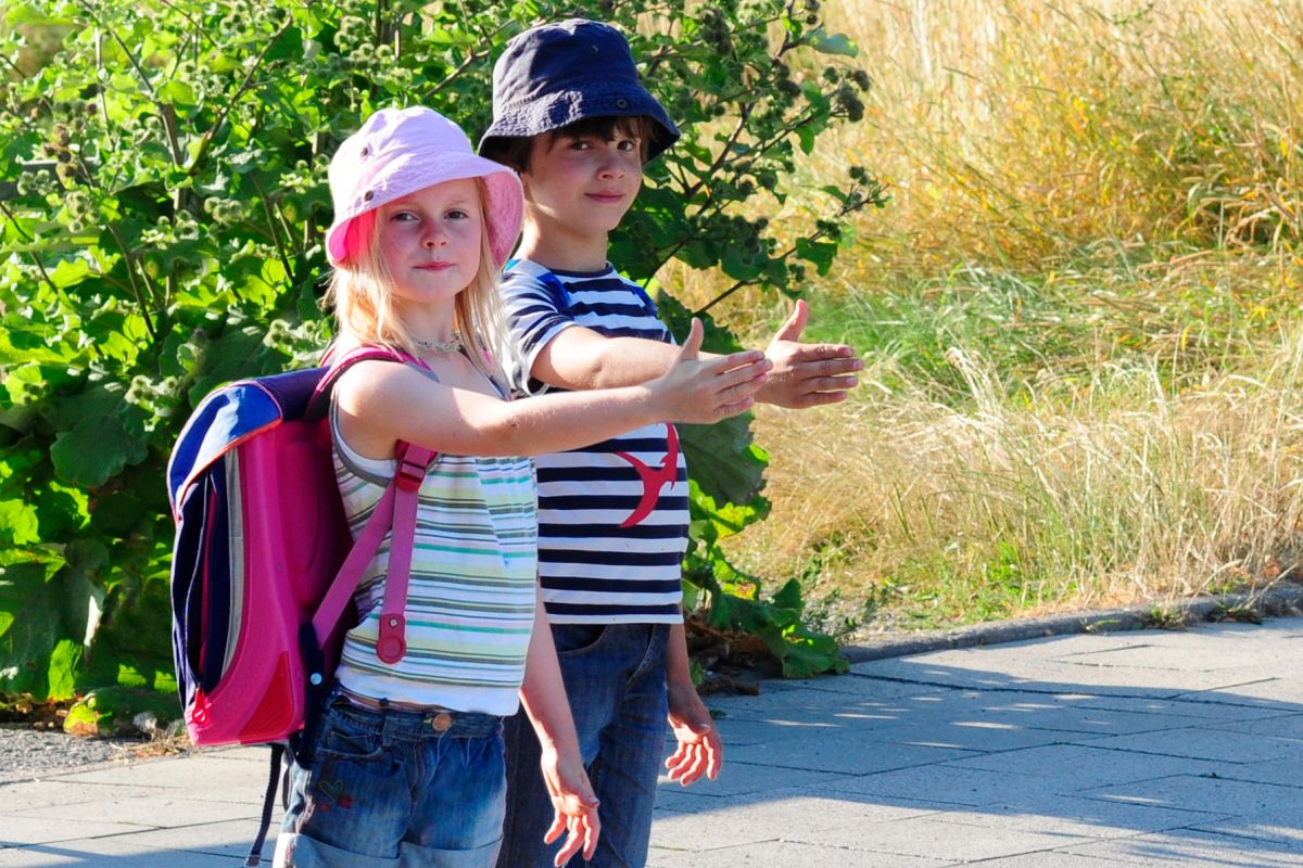 Schulkinder Kinder geben am Straßenrand Handzeichen zum Überqueren der Straßé