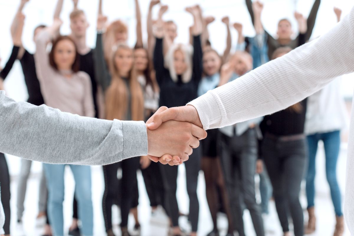Zwei Personen geben sich die Hand. Im Hintergrund jubelt eine Gruppe menschen.