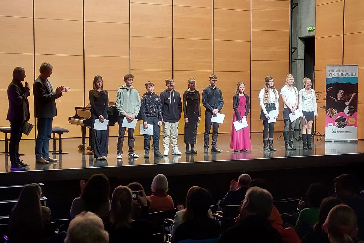 Bernhard-Krol-Wettbewerb 2025 © Ulrich Schlumberger Zehn junge Menschen mit Urkunden stehen in einer Reihe auf einer Bühne vor Publikum