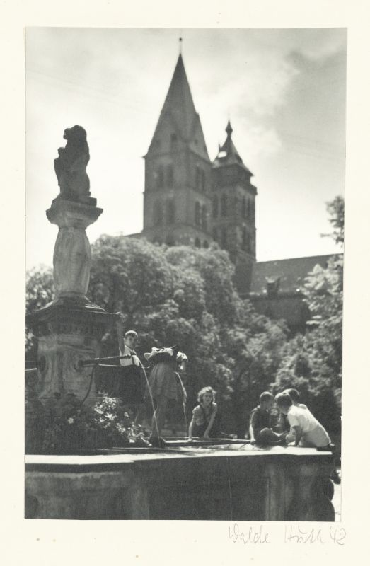 Blick auf den Löwenbrunnen mit Kindern am Marktplatz, im Hintergrund Bäume und die Türme der Stadtkirche, 1942.