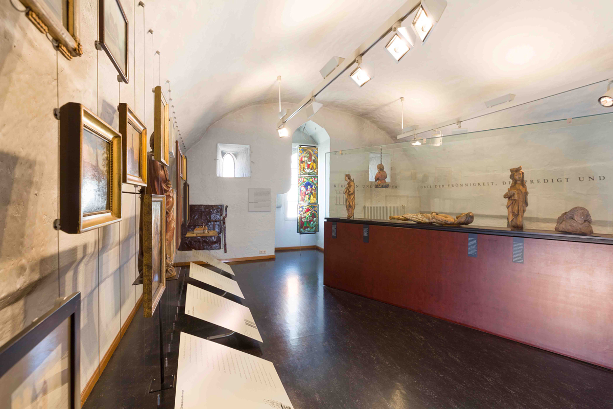 Stadtmuseum, Kirchenraum. Stadtmuseum im Gelben Haus: Raum mit Gewölbedecke, einem Buntglasfenster und mehreren kleineren Bildern.