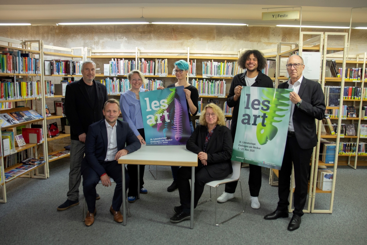 lesart 2025 Team © Kulturamt Esslingen vier Männer und drei Frauen um einen Tisch gruppiert vor Bücherregalen, sie zeigen Plakate auf denen "lesart" steht