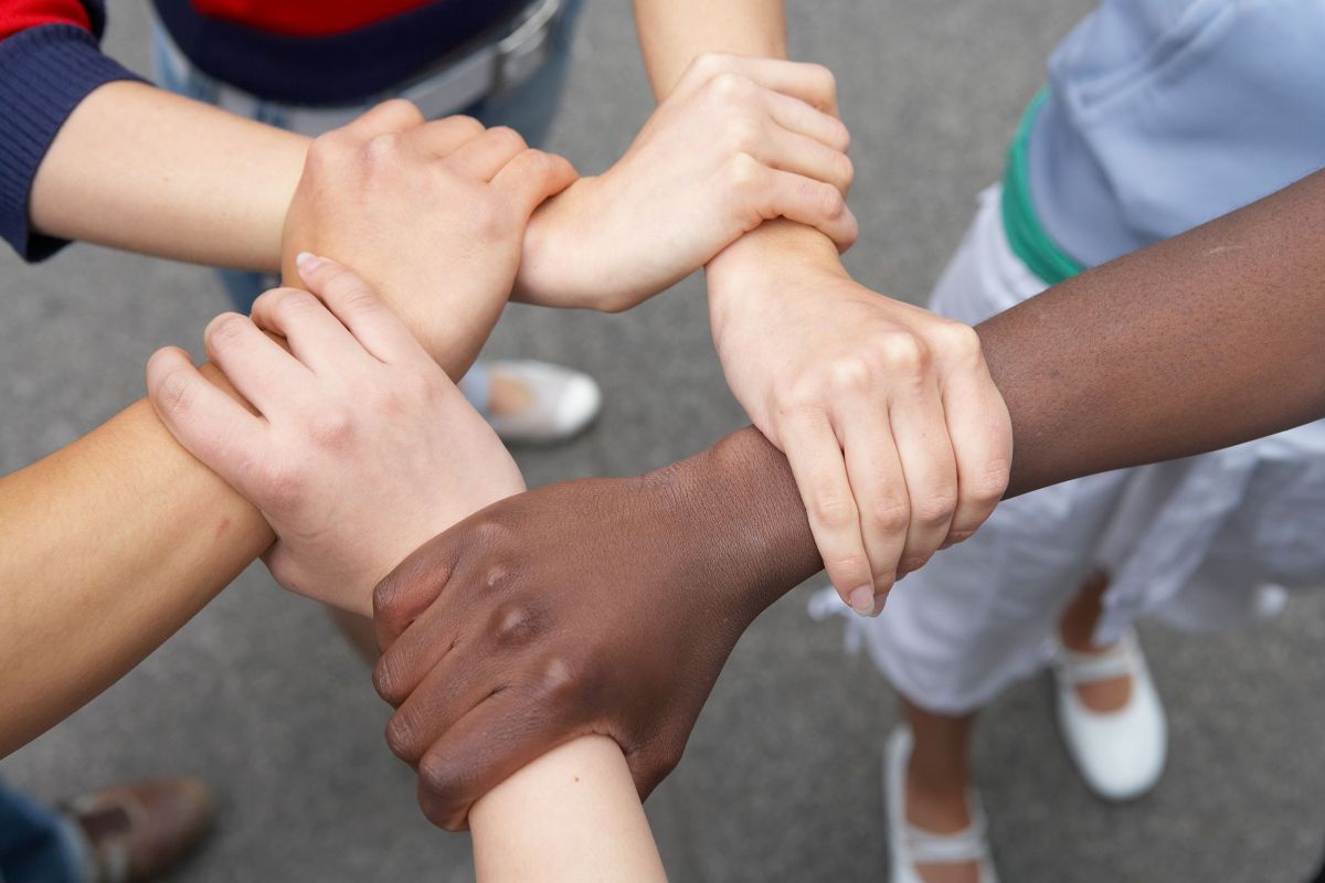Fünf verschiedene Hände greifen sich ans Handgelenk und bilden so einen Kreis.