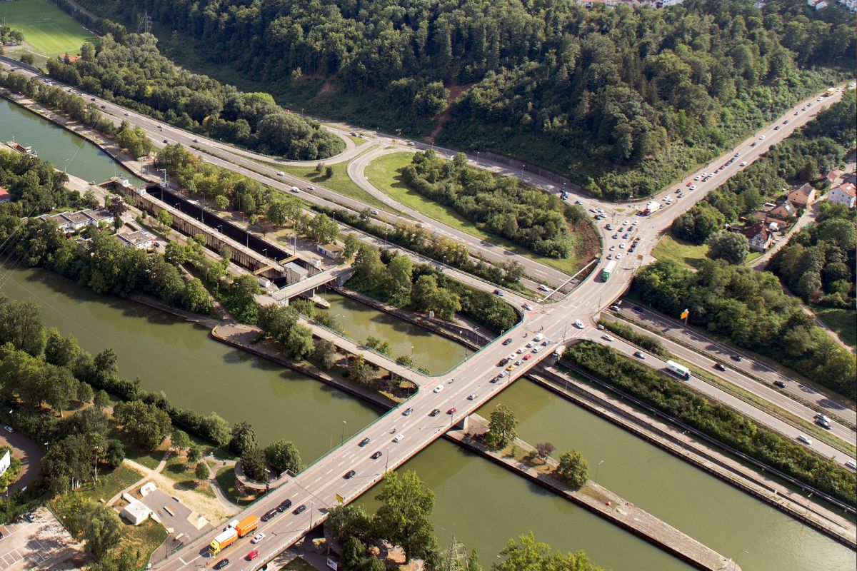 Das Lluftbild zeigt die Adenauerbrücke von oben, wie sie über die Schienen, den Neckar und die Bundesstraße führt.