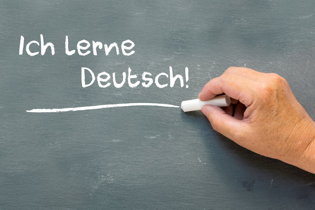 Eine Hand schreibt an eine Tafel: "Ich lerne Deutsch!"