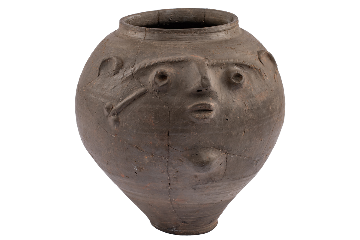 Ein bauchiges Tongefäß. Ein Gesicht und ein Phallus sind aufmodellliert.